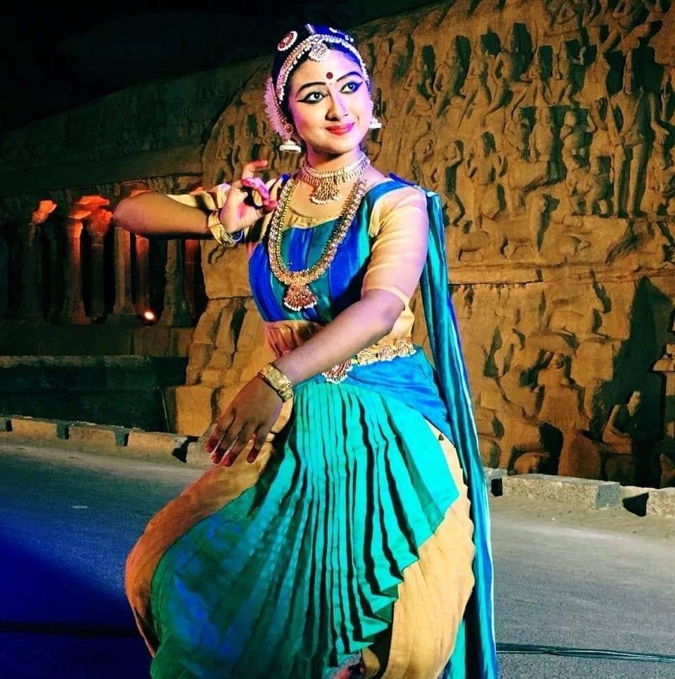Bharatanatyam dancer performing in a blue and green costume on a temple-inspired stage